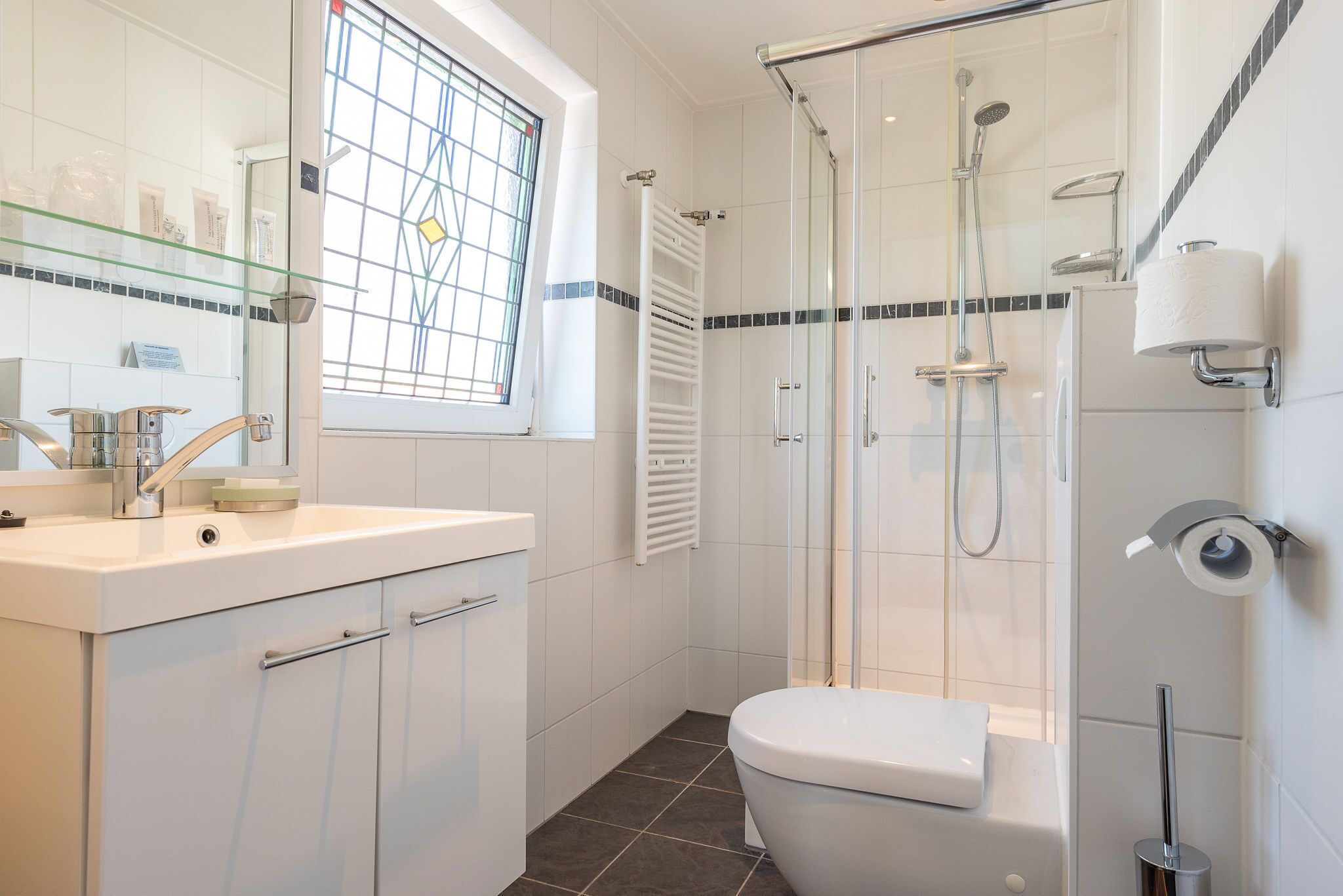 Un baño moderno con cabina de ducha de vidrio, inodoro blanco y tocador con espejo.