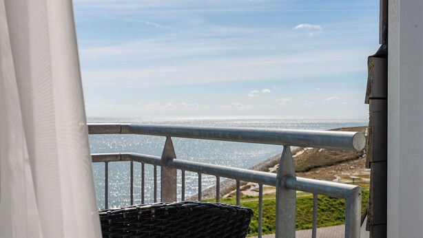 A balcony with a metal railing overlooking a coastal landscape.