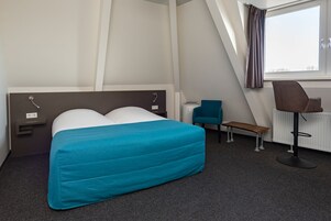 Una habitación de hotel con cama, escritorio, silla y ventana.