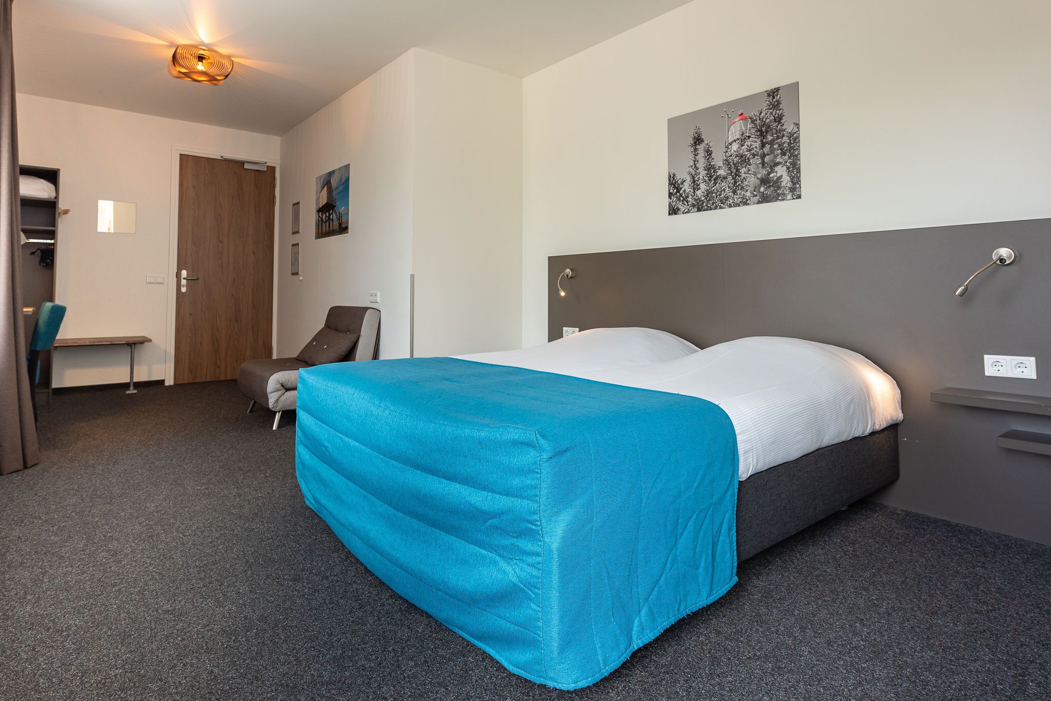 A hotel room with a bed, a desk, a chair, and a wardrobe.