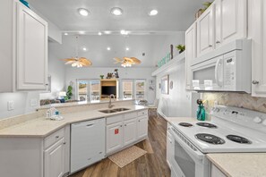 A modern kitchen with white cabinetry, a built-in dishwasher, a stainless steel sink, a double oven, and pendant lighting.