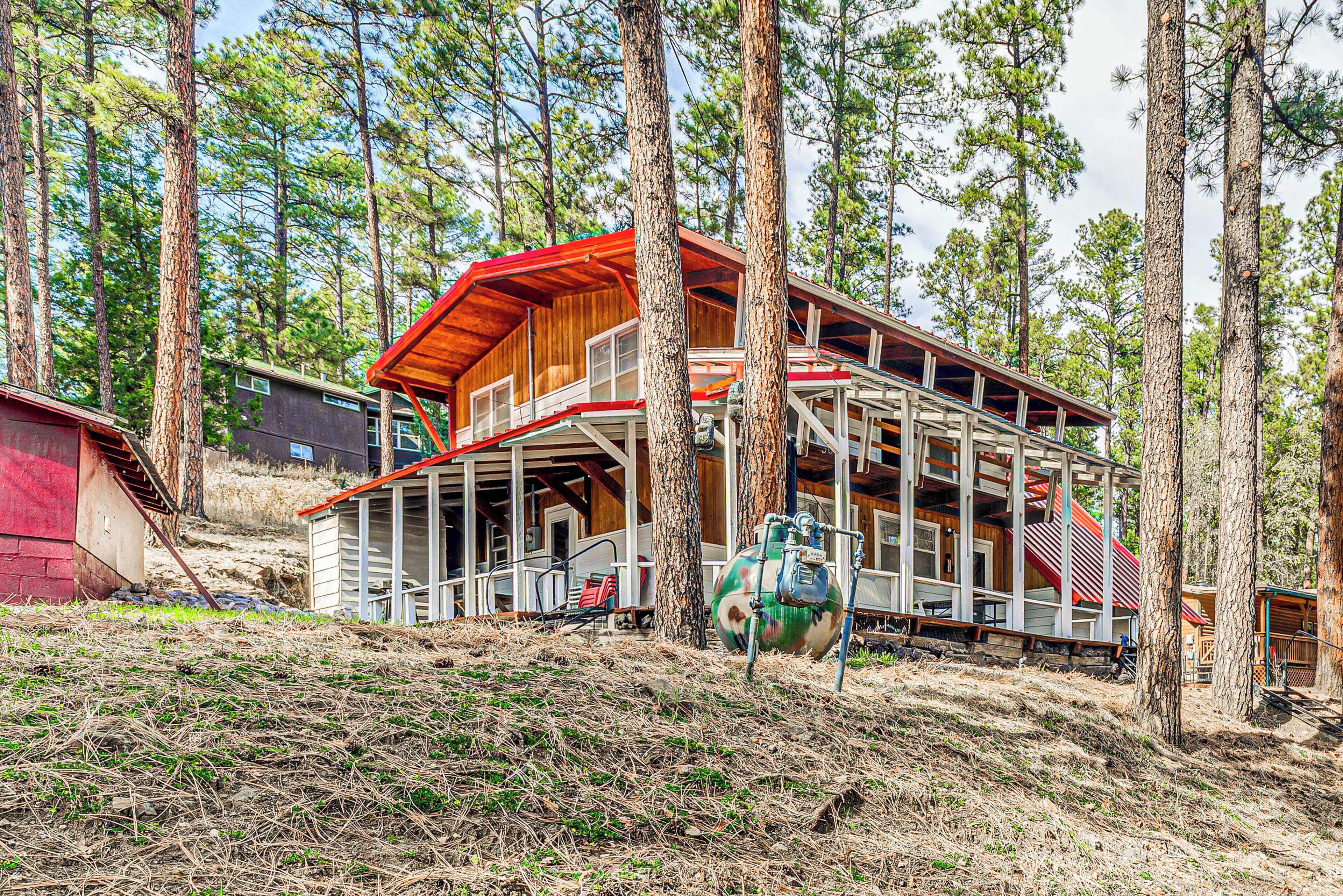 A two-story cabin with a red roof and wooden exterior, surrounded by tall pine trees.