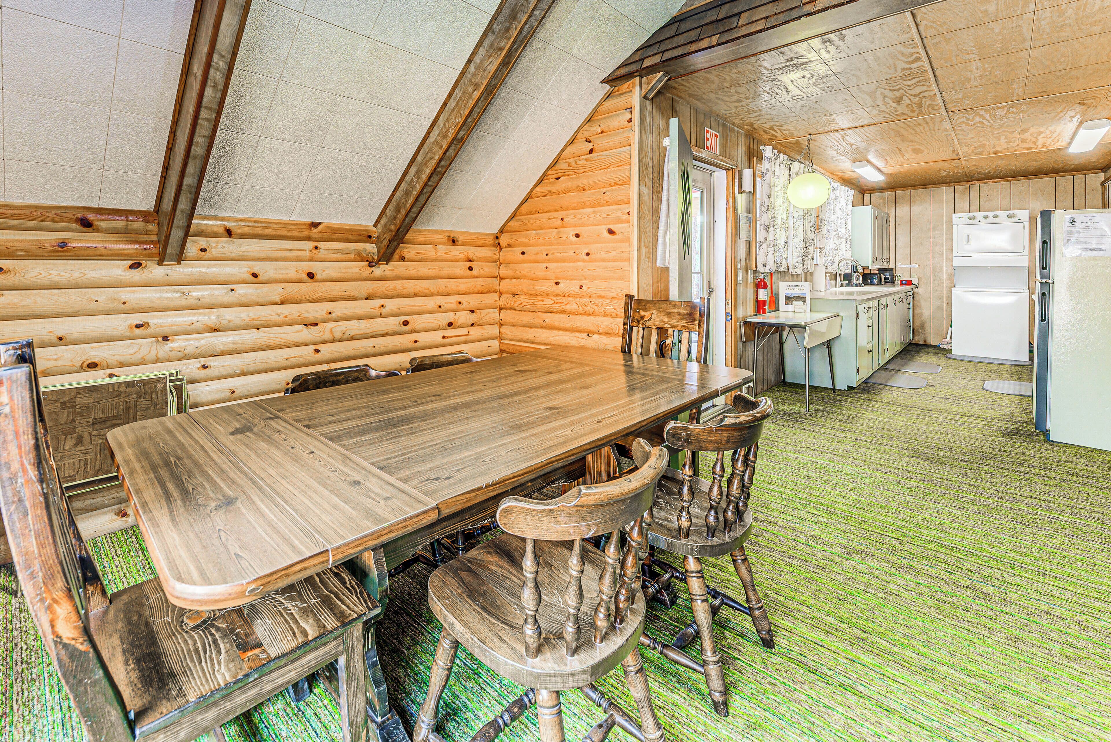 Un comedor de madera con una larga mesa y cuatro sillas, una cocina con electrodomésticos y un suelo cubierto de alfombra verde.