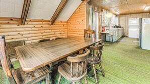 Un comedor de madera con una larga mesa y cuatro sillas, una cocina con electrodomésticos y un suelo cubierto de alfombra verde.