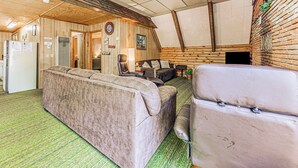Interior acogedor de una cabaña con sofá, sillón, mesa de comedor y zona de cocina.