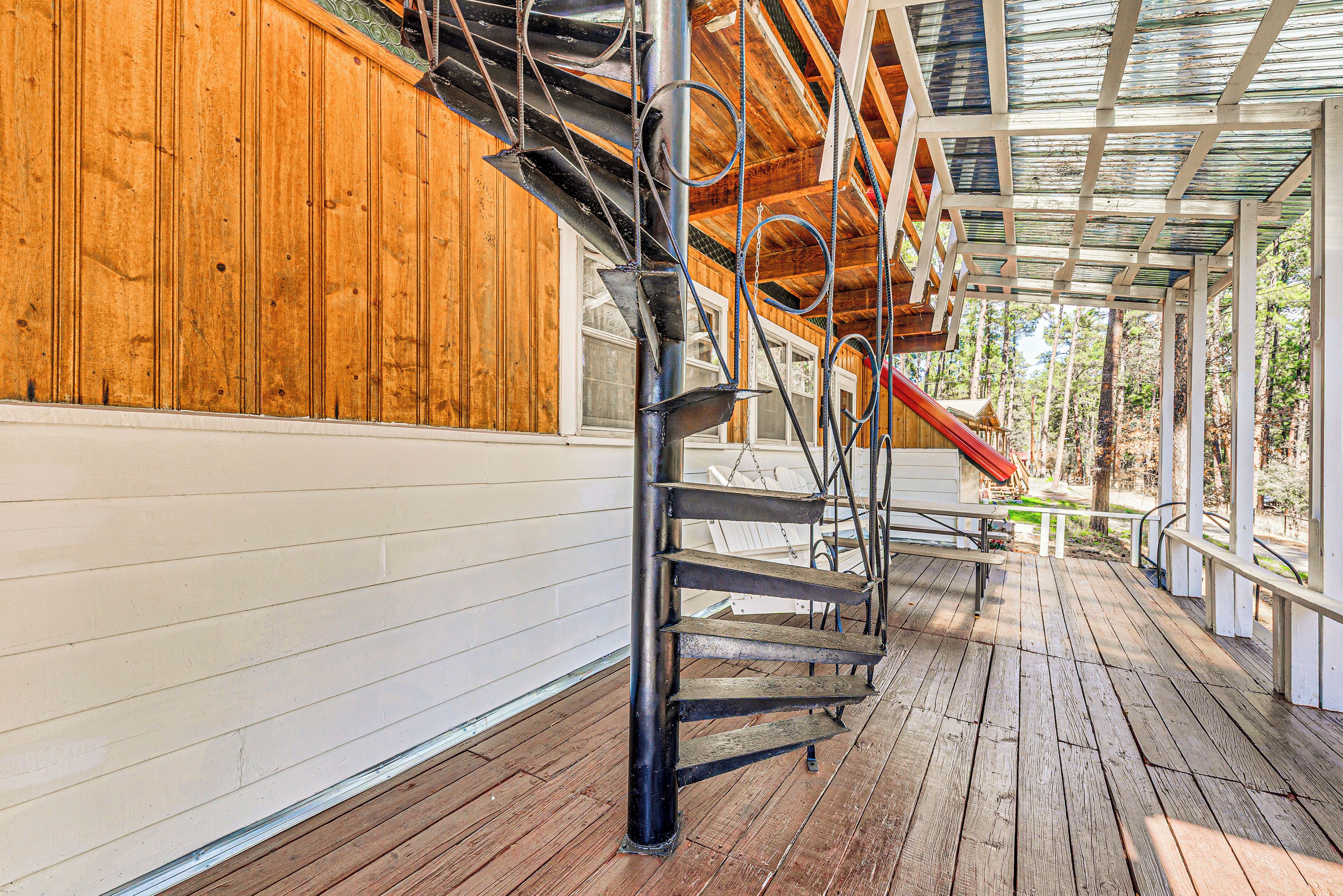 A wooden exterior with a metal staircase and a red slide leading to a covered area with a view of trees.