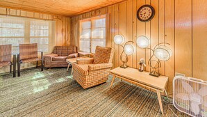Una habitación acogedora con paredes de madera, un sillón escocés, una mesita con lámparas y un reloj en la pared.