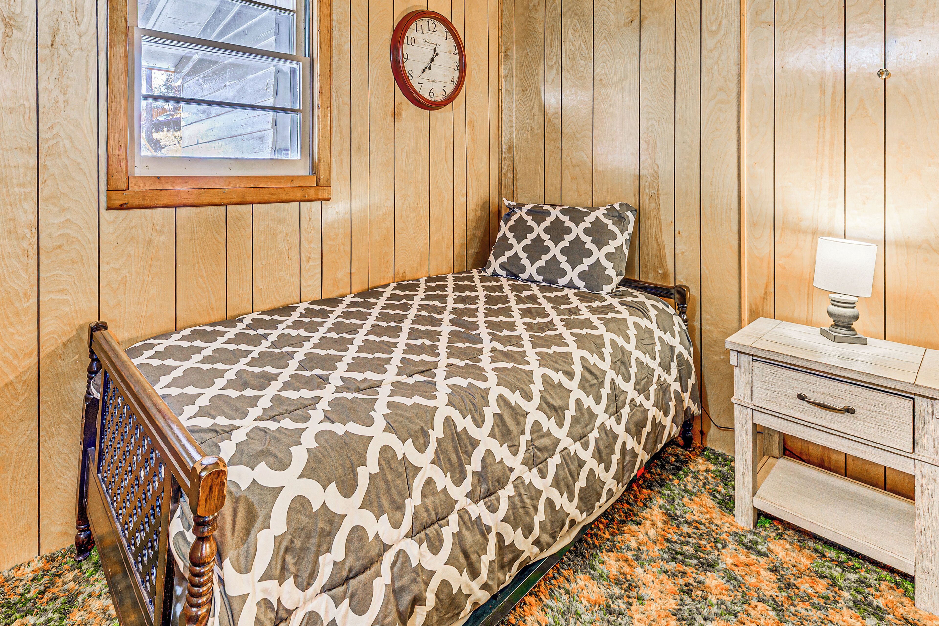 A bedroom with a wooden paneled wall, a bed with a patterned bedspread, a bedside table with a lamp, and a wall clock.