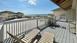 Eine Holzterrasse mit Blick auf Strand und Meer, weiße Geländer und ein klarer Himmel.