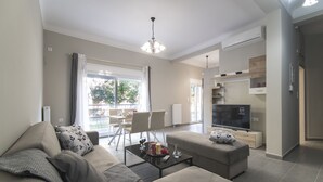 A modern living room with a sofa, coffee table, and TV. There is a dining area in the background with chairs and a table. - Down Town Modern Apartments (Athens)
