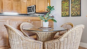A kitchen with wooden cabinets, a microwave, a dining table with wicker chairs, and two wall-mounted paintings.