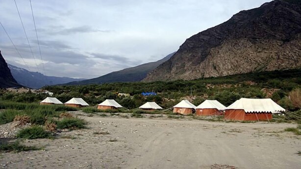 A row of tents in a mountainous area with a dirt road in the foreground. - Jispa Journeys - Campsite (Lahul)