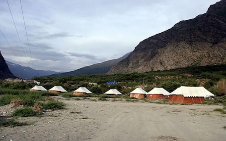 A row of tents in a mountainous area with a dirt road in the foreground.