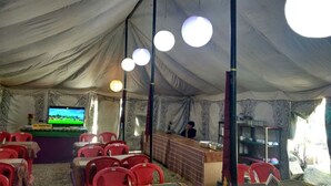 A tented dining area with red chairs, a counter, and a television screen. - Jispa Journeys - Campsite (Lahul)