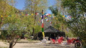 A tent with red chairs and a flagpole with colorful flags. - Jispa Journeys - Campsite (Lahul)