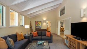 Ein geräumiges Wohnzimmer mit hohen Decken, einer Couch, einem Couchtisch und einem Fernseher.