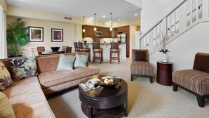 A spacious living area with a sofa, armchairs, a coffee table, and a staircase leading to an upper level. - 2-Story w/Modern Kitchen–Halii Kai at Waikoloa 1G (WAIKOLOA)