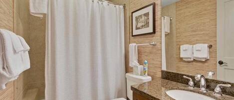 A bathroom with a shower curtain, toilet, sink, and a framed picture on the wall.