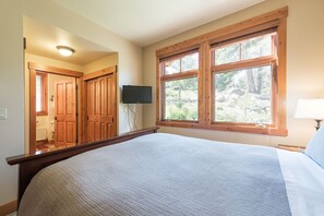 Quarto com cama grande, portas de madeira, televisão e janela com vista para árvores.