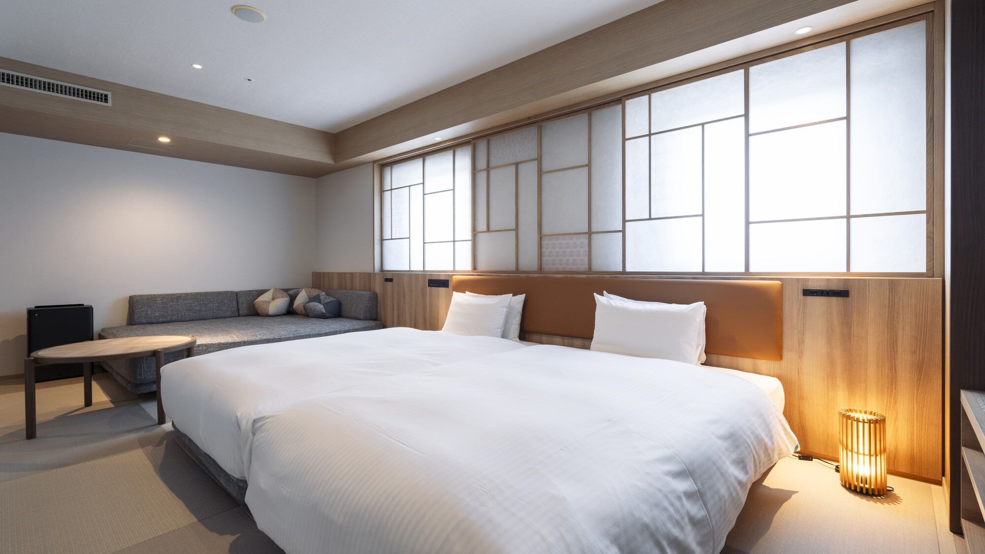 A hotel room with a large bed, a sofa, a small table, and a large window with a view.