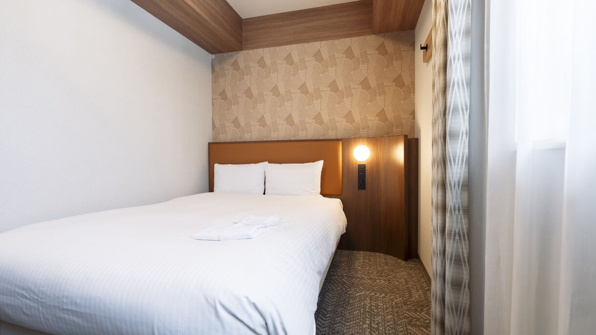 Una habitación de hotel con cama, cabecera con lámpara y pared con diseño, además de una ventana con cortinas.