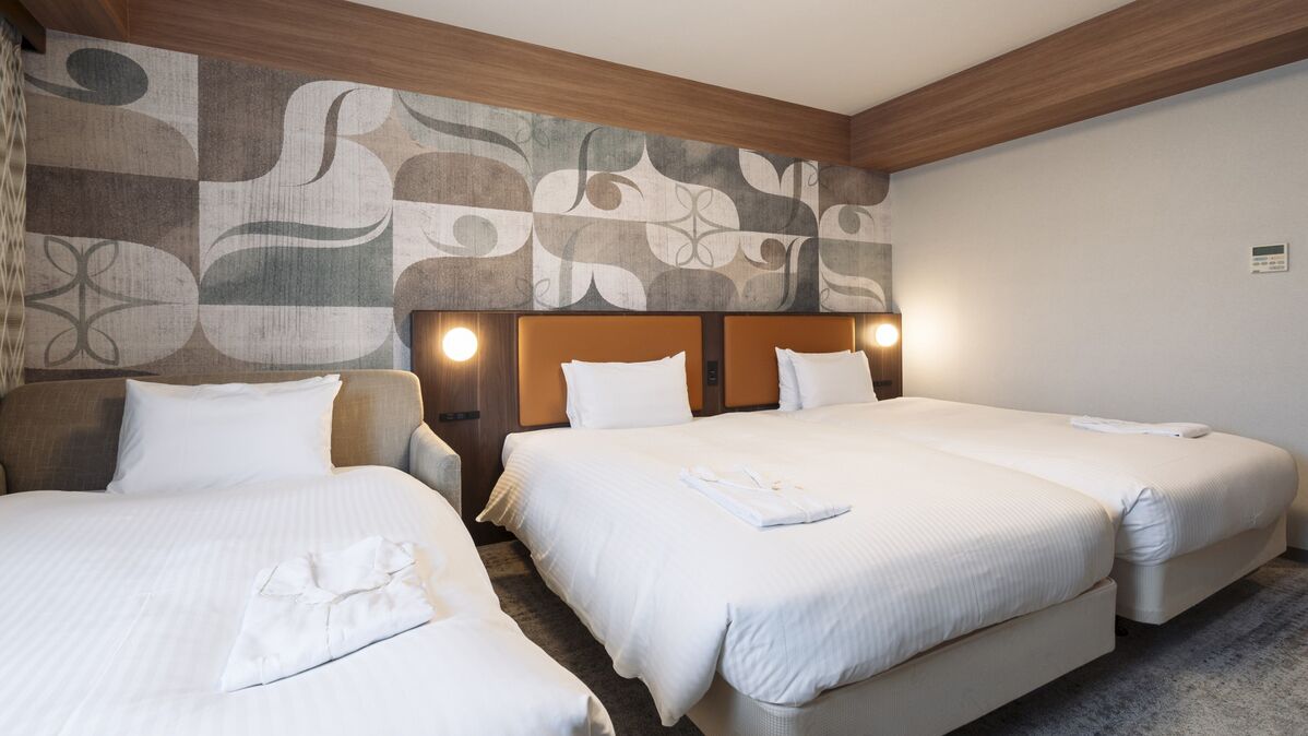 Una habitación de hotel con tres camas, cabecera de madera y pared con diseño.