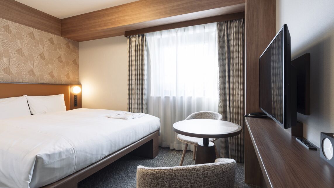 Habitación de hotel con cama, una mesita redonda, televisión y ventana con cortinas.