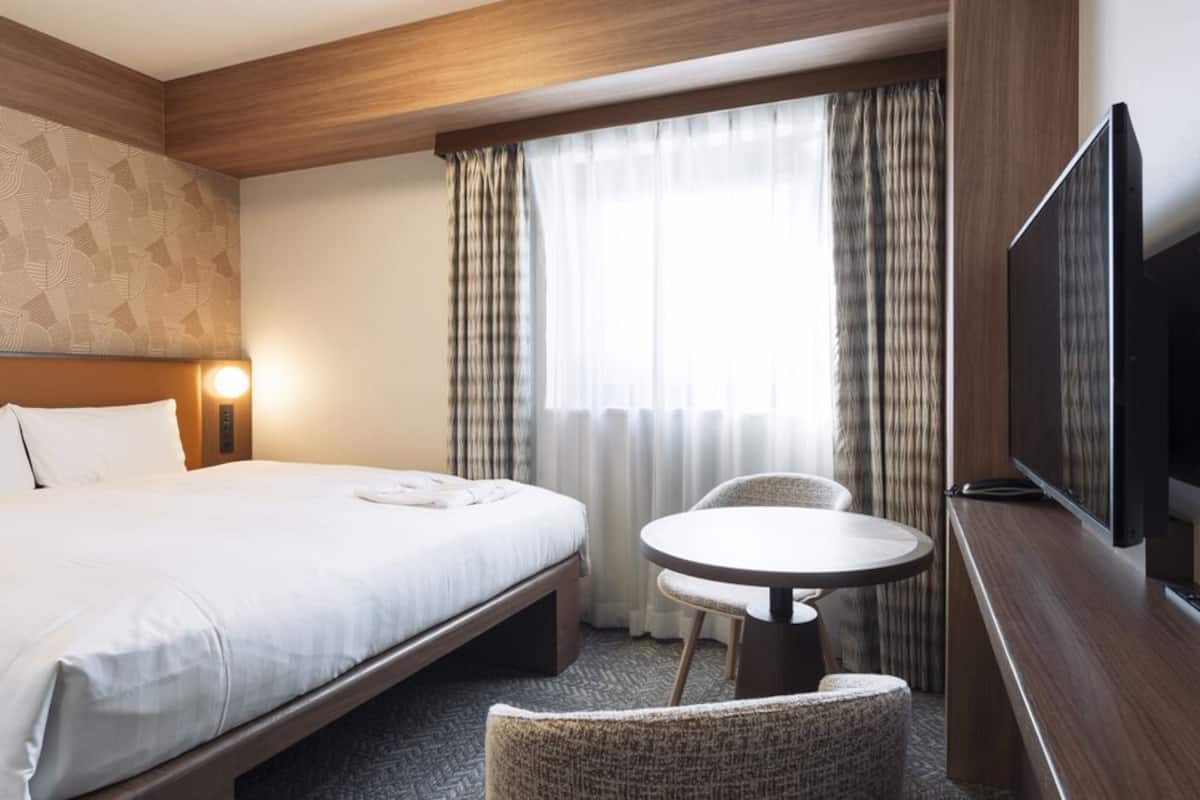 Habitación de hotel con cama, una mesita redonda, televisión y ventana con cortinas.
