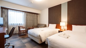 Hotellihuone, jossa on kaksi sänkyä, työpöytä, tuoli, televisio ja ikkuna, jossa on verhot.