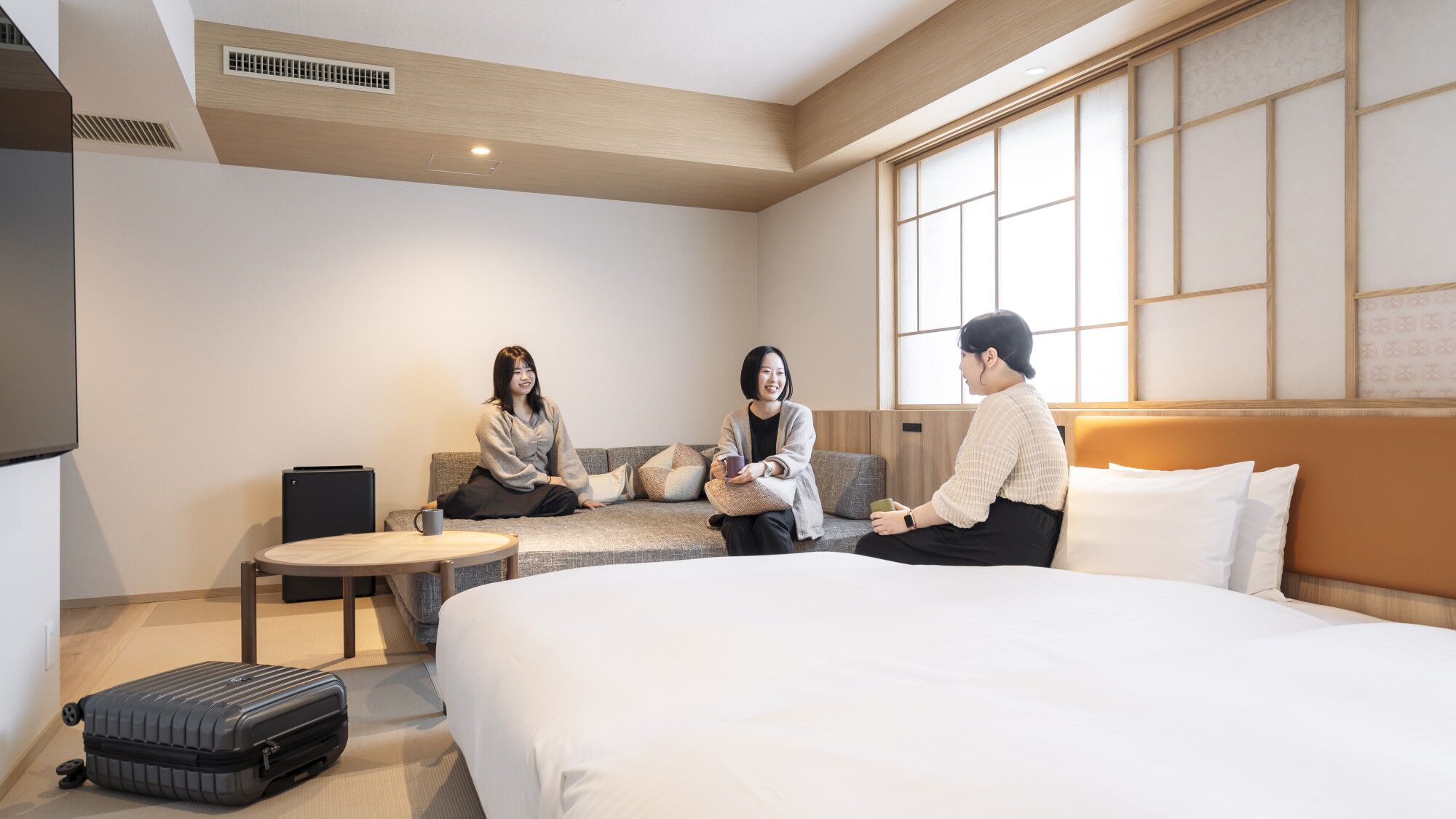 A hotel room with a bed, a sofa, a small table, and a suitcase.