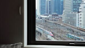 A window view of a train station with multiple tracks and trains, surrounded by modern buildings. - Keio Presso Inn Otemachi (Tokyo)