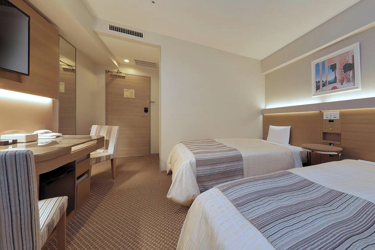 A hotel room with two beds, a desk with a chair, a flat-screen TV, and a painting on the wall.