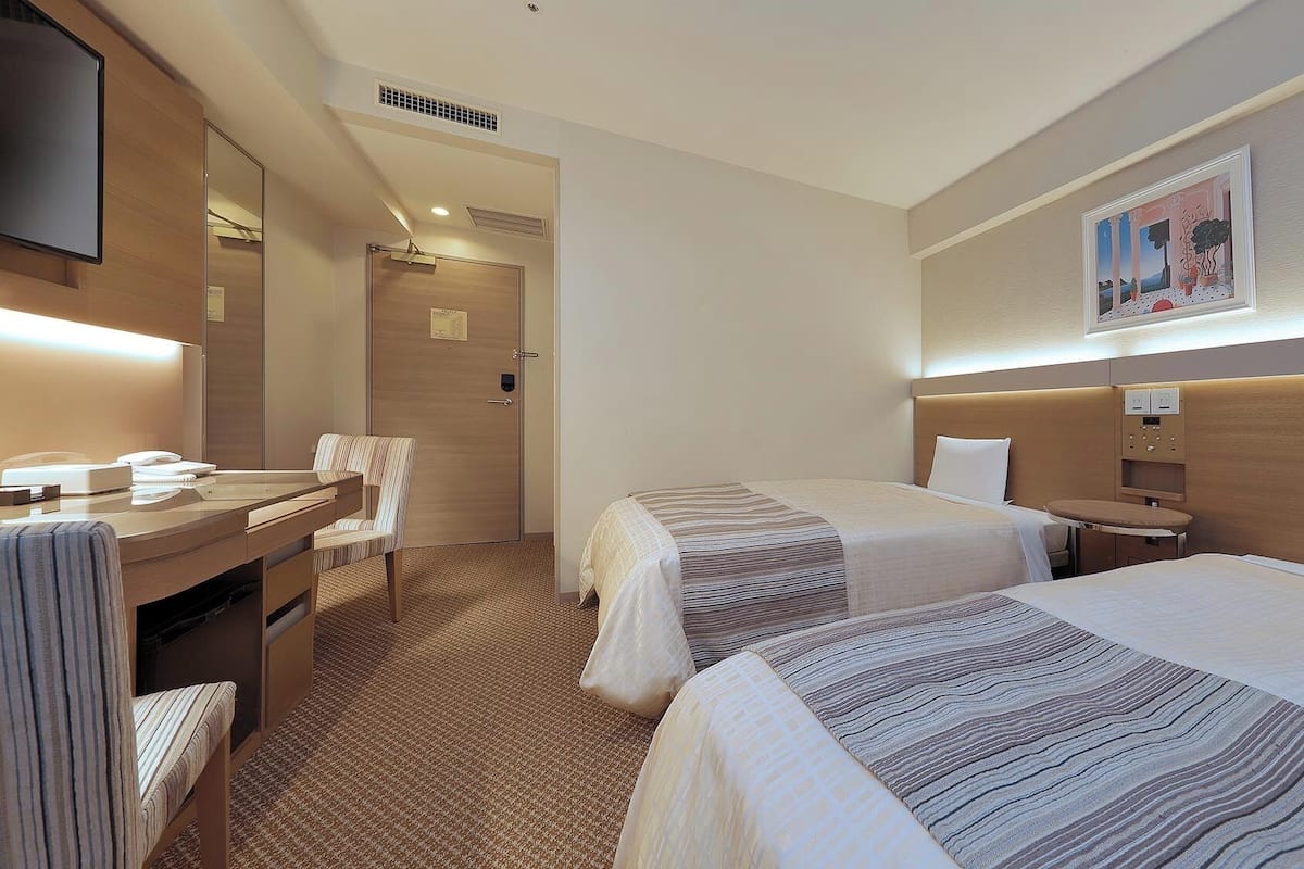A hotel room with two beds, a desk with a chair, a flat-screen TV, and a painting on the wall.