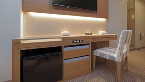 A hotel room with a wooden desk, a flat-screen TV mounted above it, a built-in mini-fridge, a chair, and a bedside table with a lamp. - Keio Presso Inn Otemachi (Tokyo)