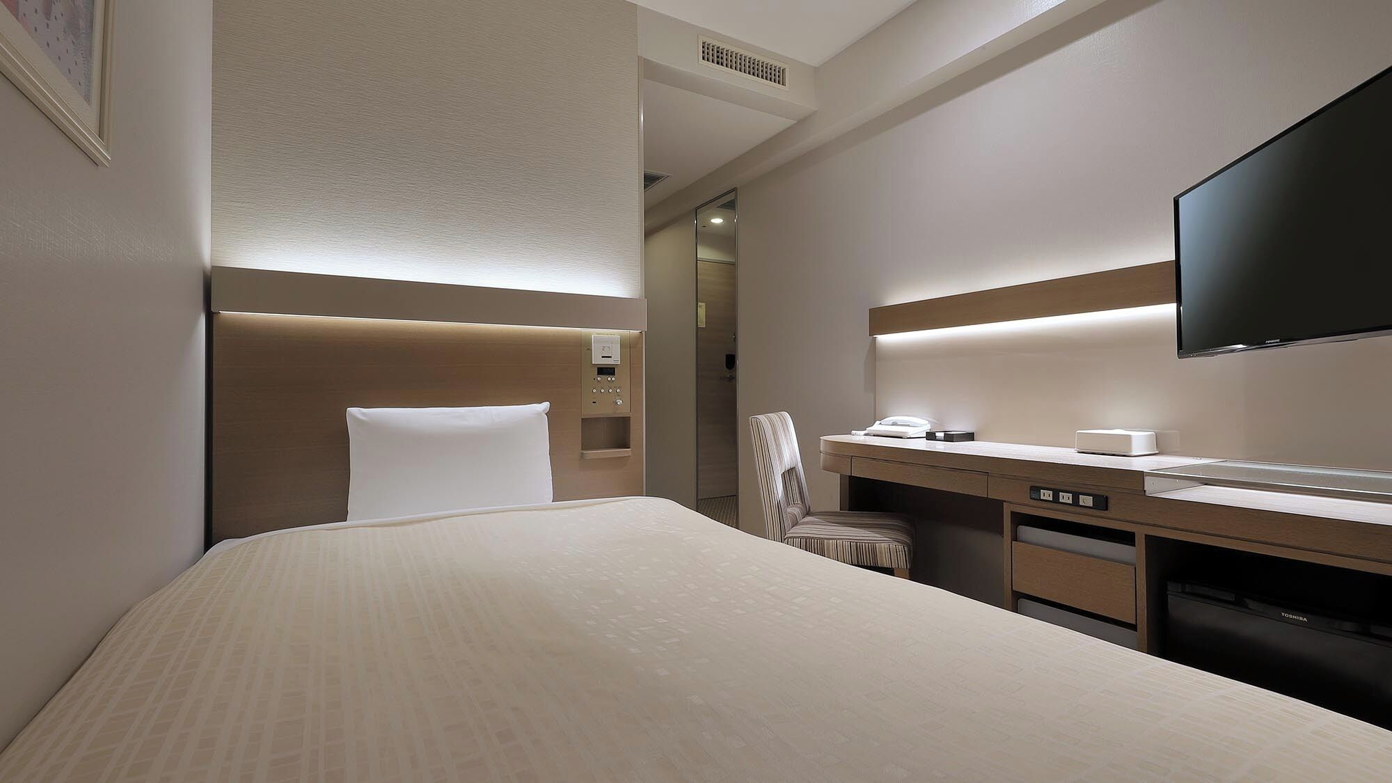 A hotel room with a bed, a desk, a chair, a flat-screen TV, and a mirror.