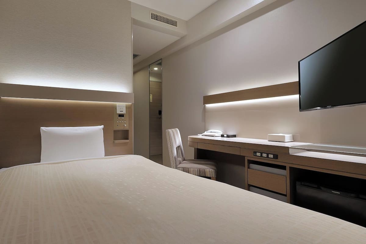 A hotel room with a bed, a desk, a chair, a flat-screen TV, and a mirror.