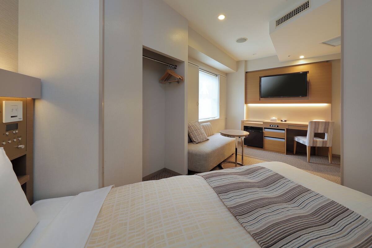A hotel room with a bed, a desk, a chair, a TV, and a wardrobe.