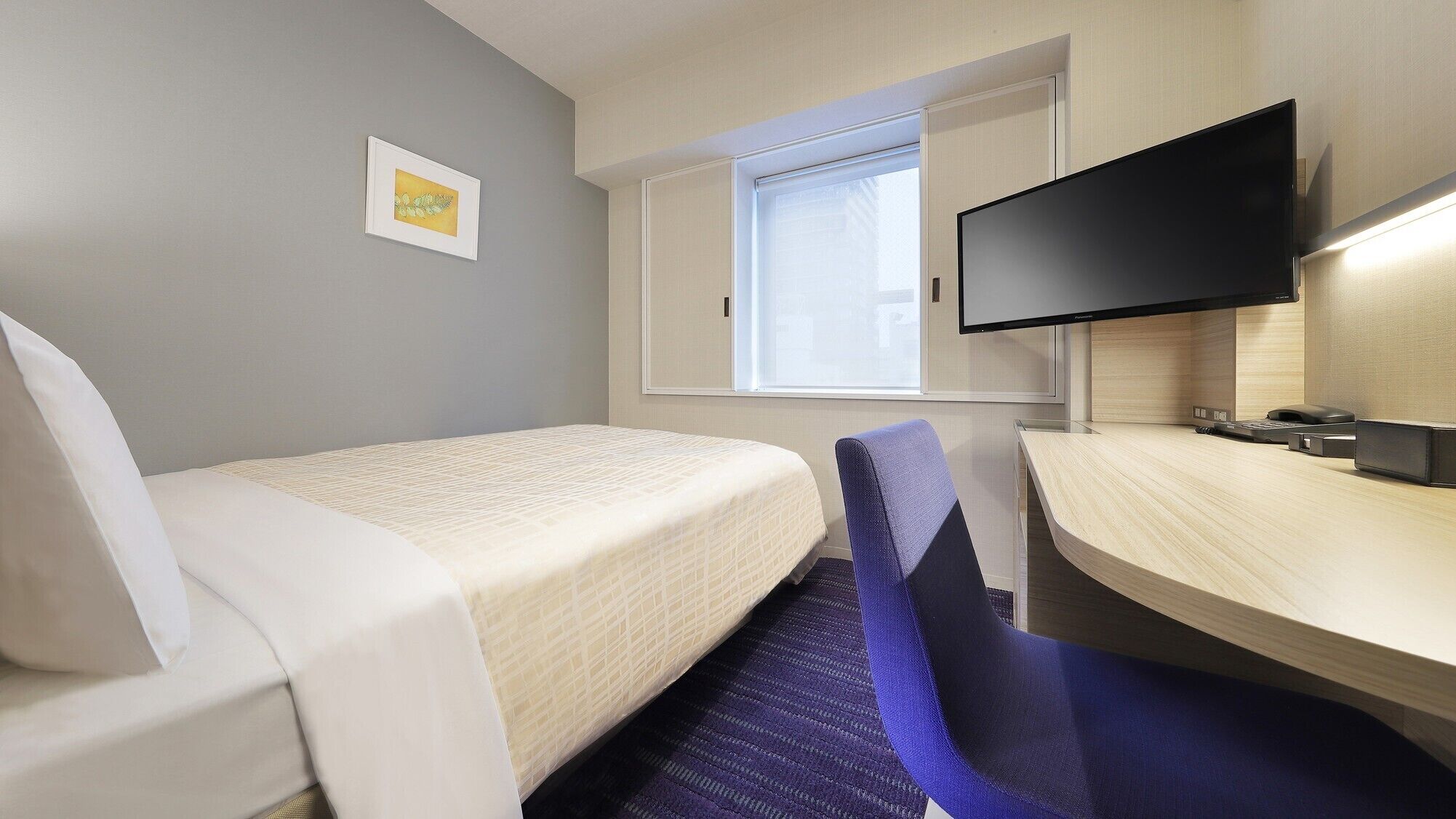 Una habitación de hotel con cama, escritorio, silla, televisor y ventana.