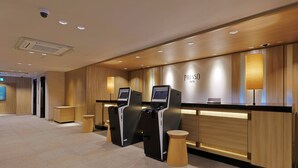 A hotel reception area with a wooden finish, a reception desk, a digital kiosk, and a wall-mounted lamp. - Keio Presso Inn Gotanda (Tokyo)