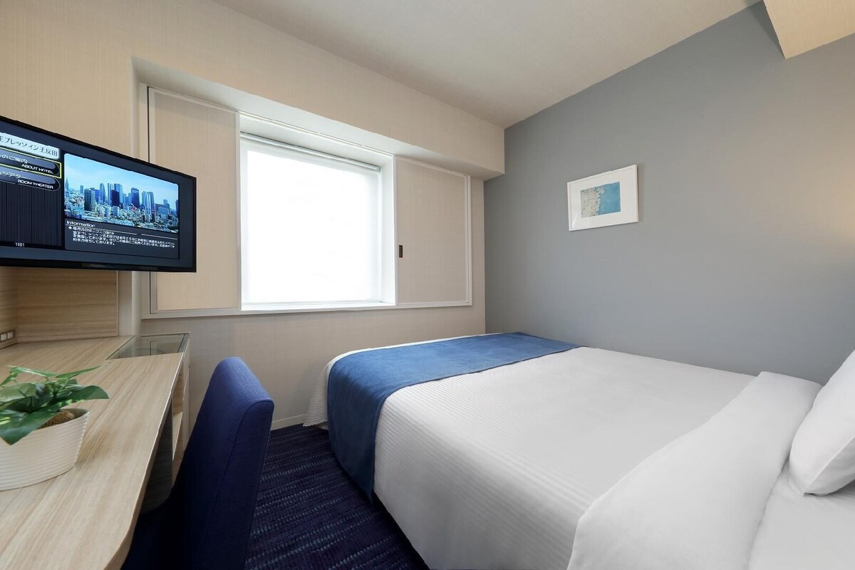 Hotellihuone, jossa on sänky, työpöytä, televisio ja ikkuna.