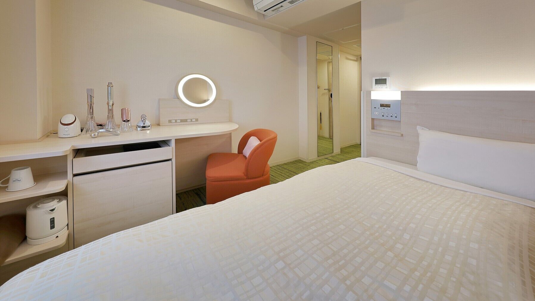 Habitación de hotel con cama, escritorio con espejo, una silla, inodoro y zona de ducha.