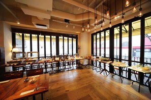 Un restaurant doté de nombreuses tables, de luminaires suspendus et de grandes fenêtres.
