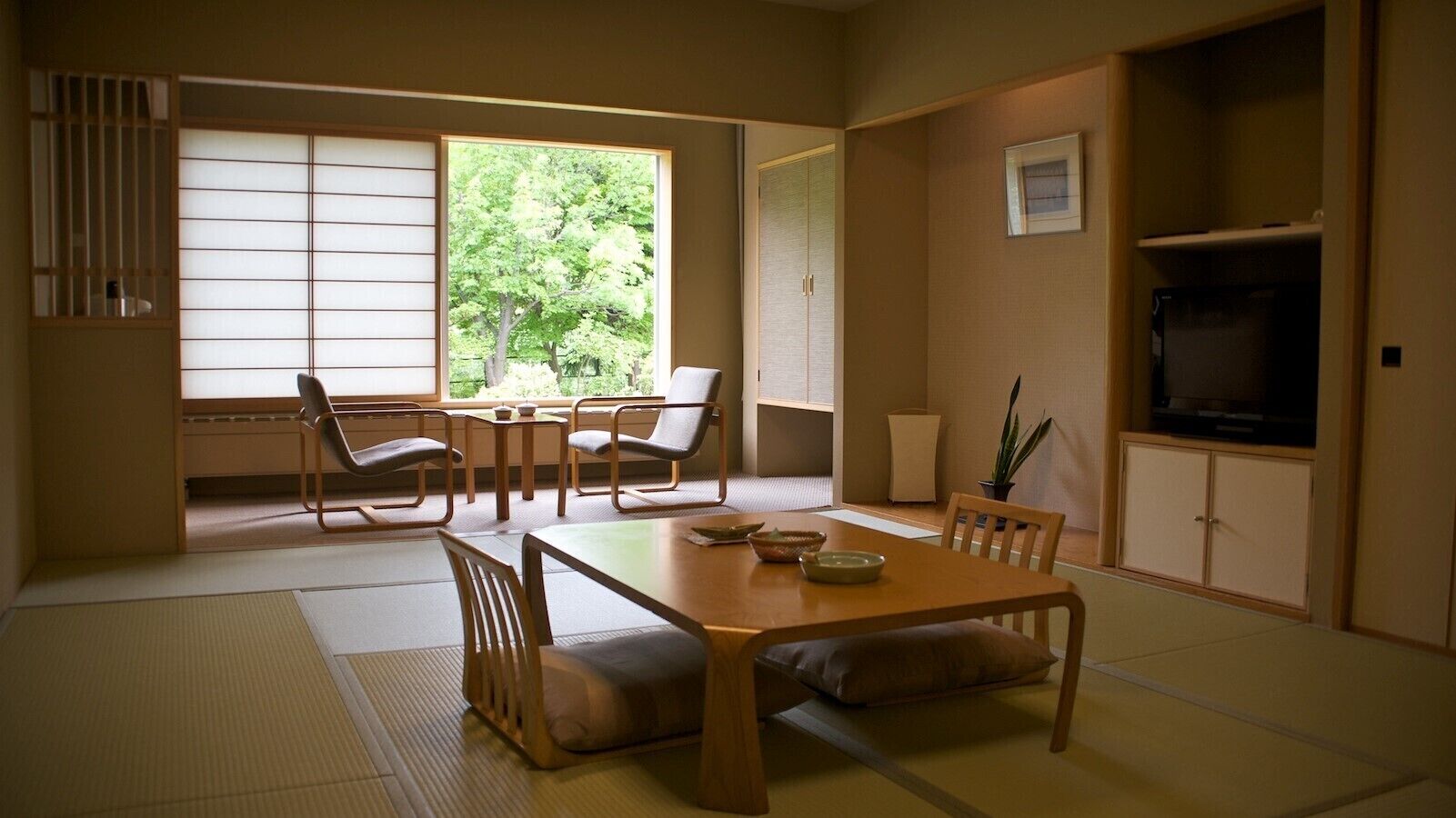 Ein traditioneller japanischer Raum mit Tatami-Boden, einem niedrigen Tisch mit Kissen und Schiebetüren, die auf einen Balkon führen.