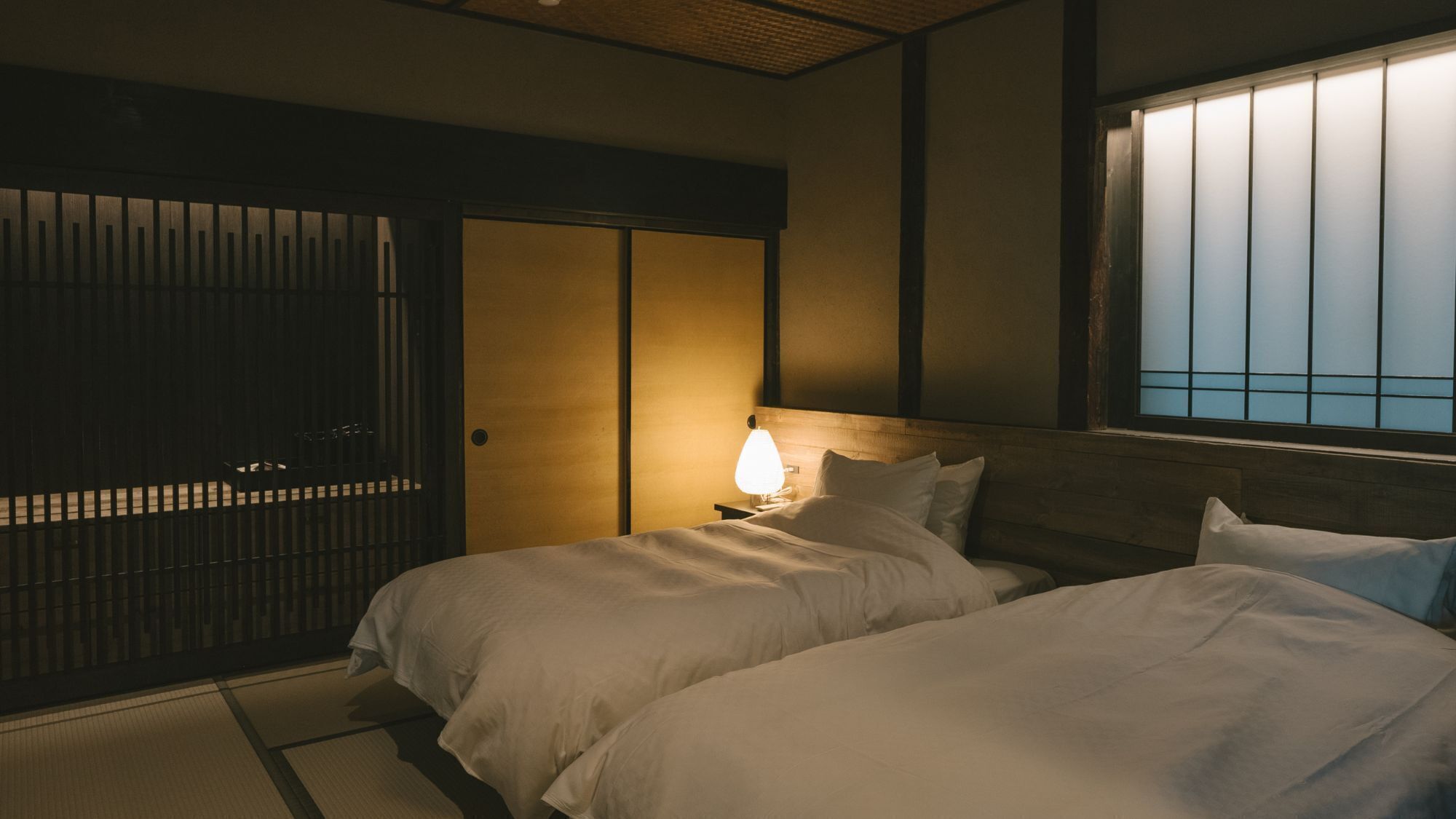 Una habitación tradicional japonesa con suelo de tatami, un shoji y una cama con cabecera de madera.