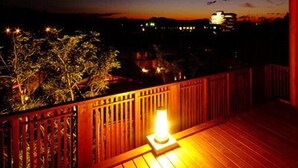A wooden deck with a railing, a lit lantern, and a view of a cityscape at dusk.