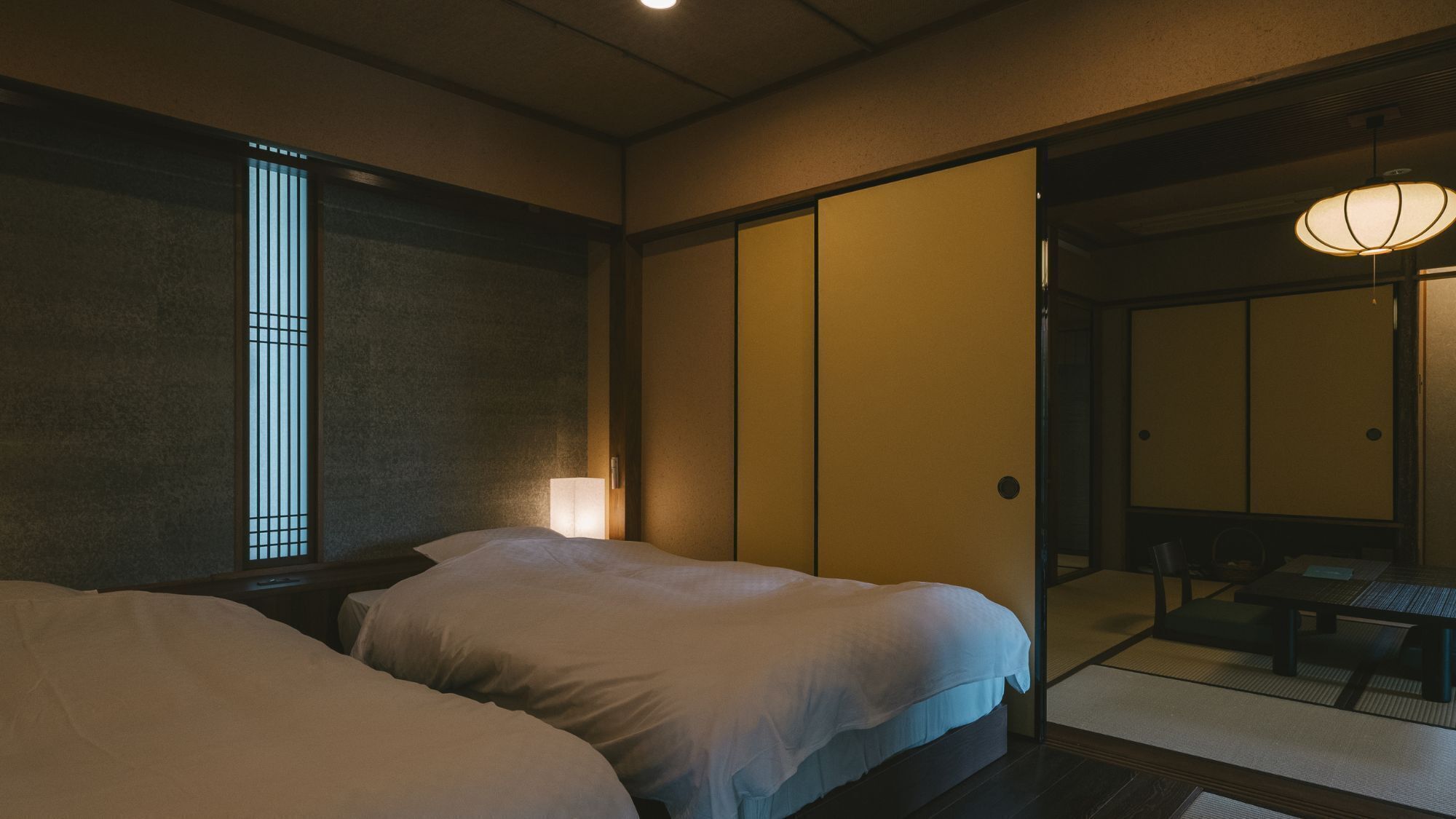 Una habitación al estilo japonés tradicional con dos camas, un puertas correderas y una pequeña mesa con sillas.