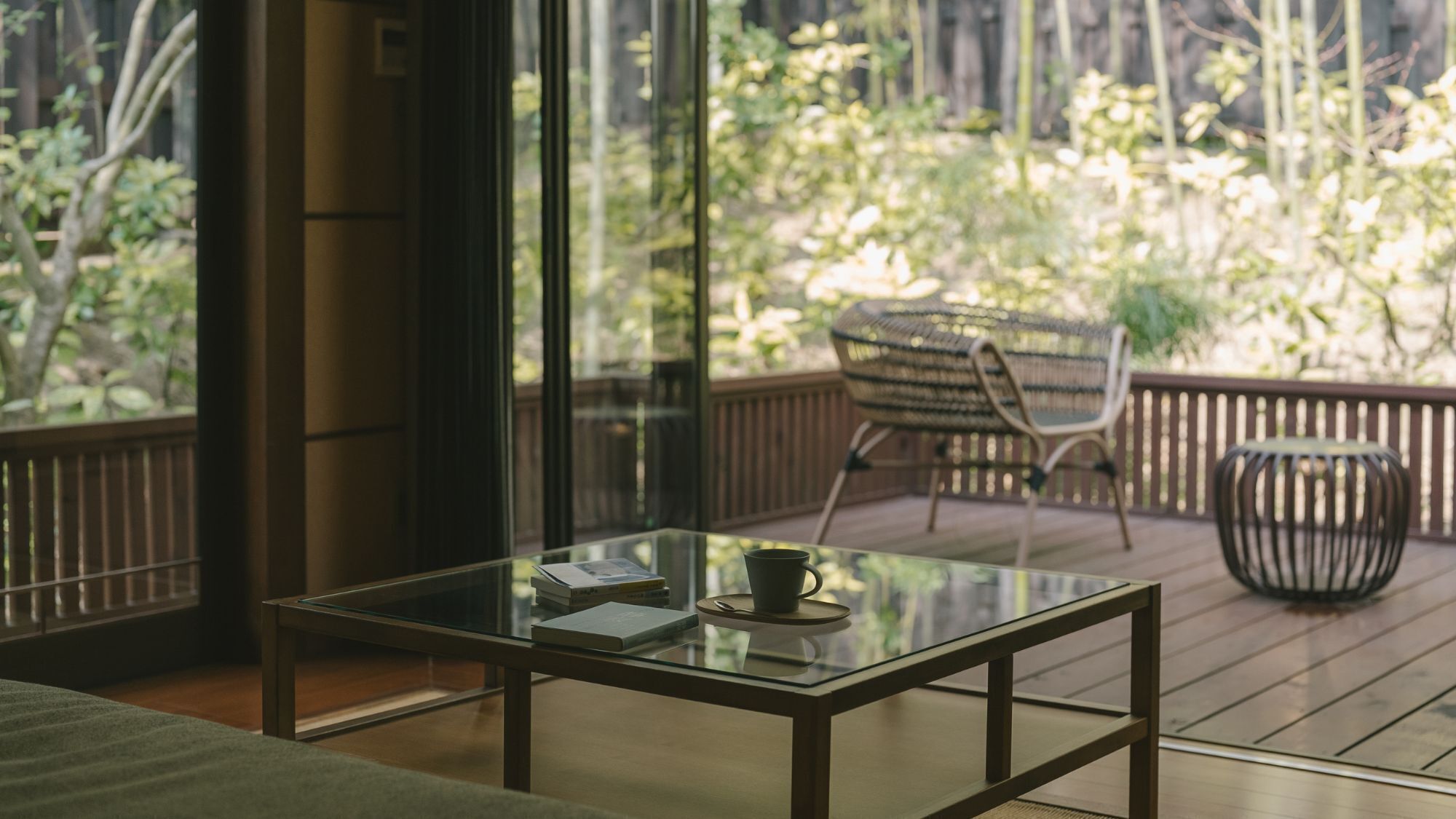 Una habitación moderna con una mesa de vidrio, una silla y vistas a una terraza de madera y vegetación exterior.