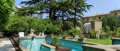 A swimming pool with a waterfall feature, surrounded by lush greenery and a wooden deck.