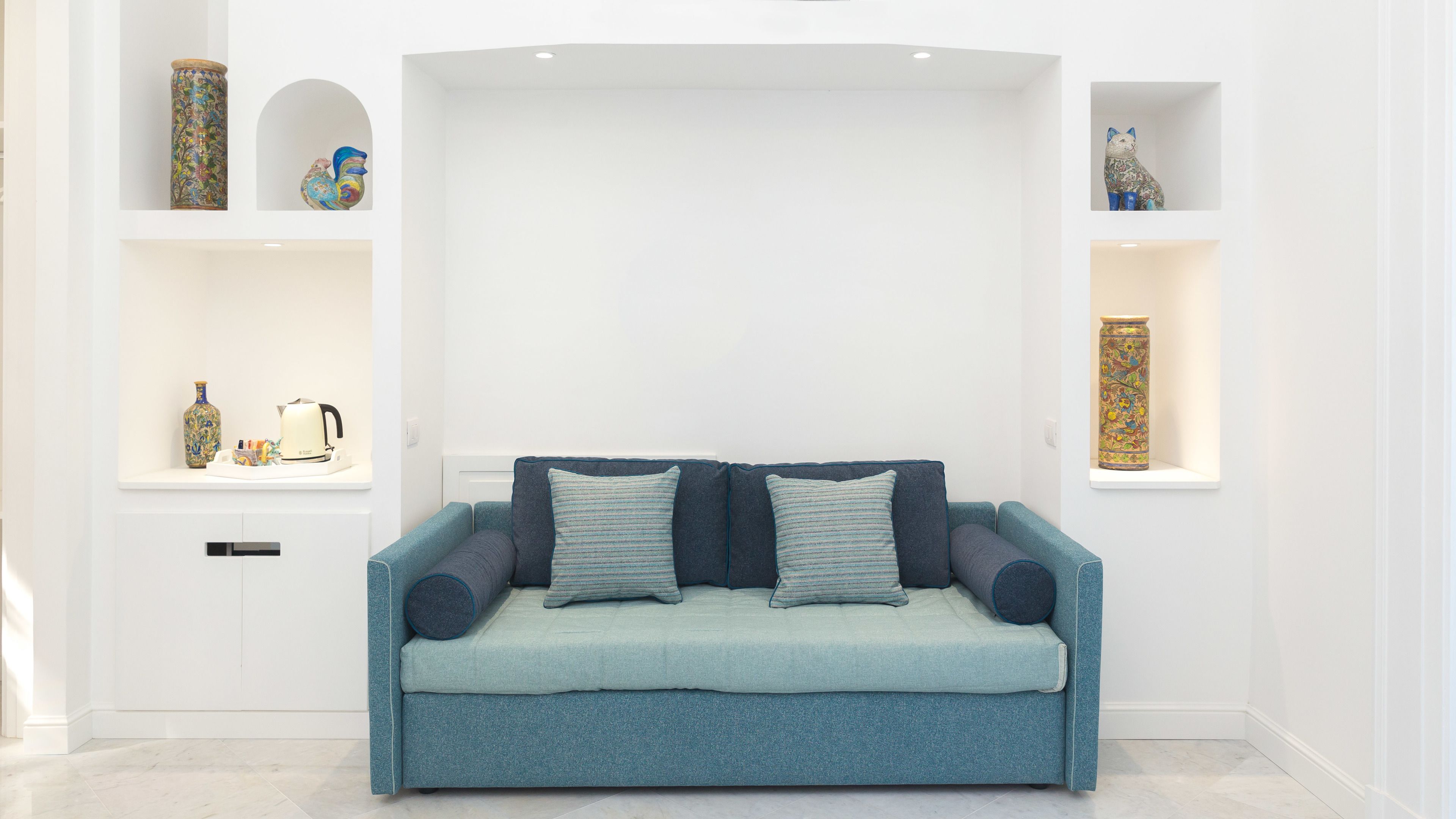 Una sala moderna con un sofá azul aguamarina, dos cojines y objetos decorativos sobre estanterías blancas.