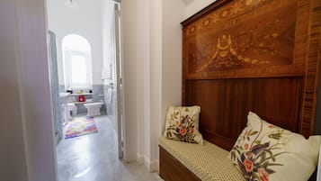 Ein Schlafzimmer mit hölzernem Kopfteil, einem farbenfrohen Teppich und Blick ins Badezimmer.